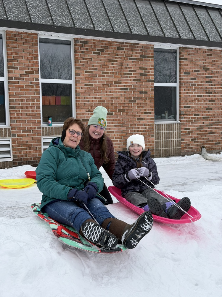 staff and student smiling and sledding 