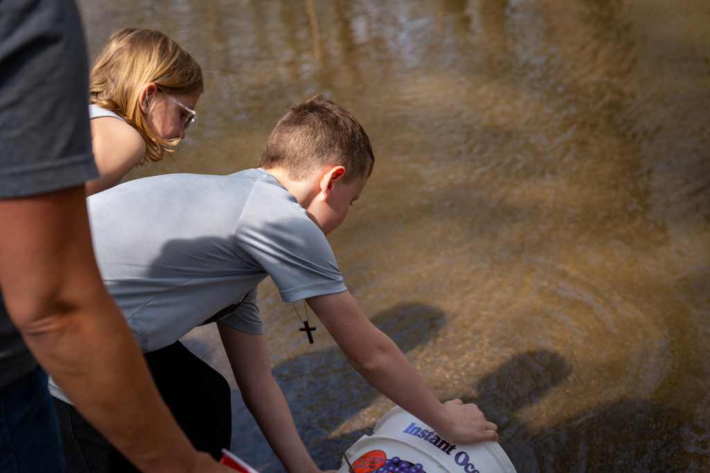 Elementary students scooping water from the river
