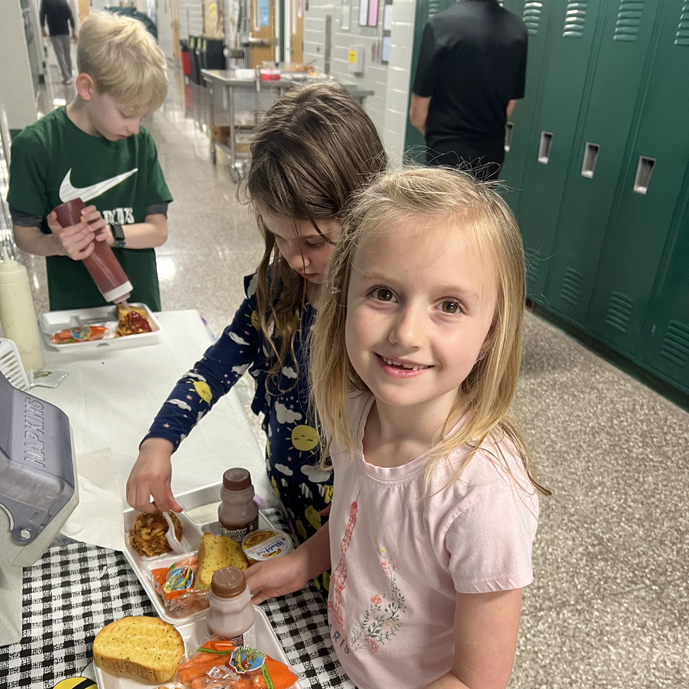 An elementary-aged girl smiles at the camera with her lunch tray.