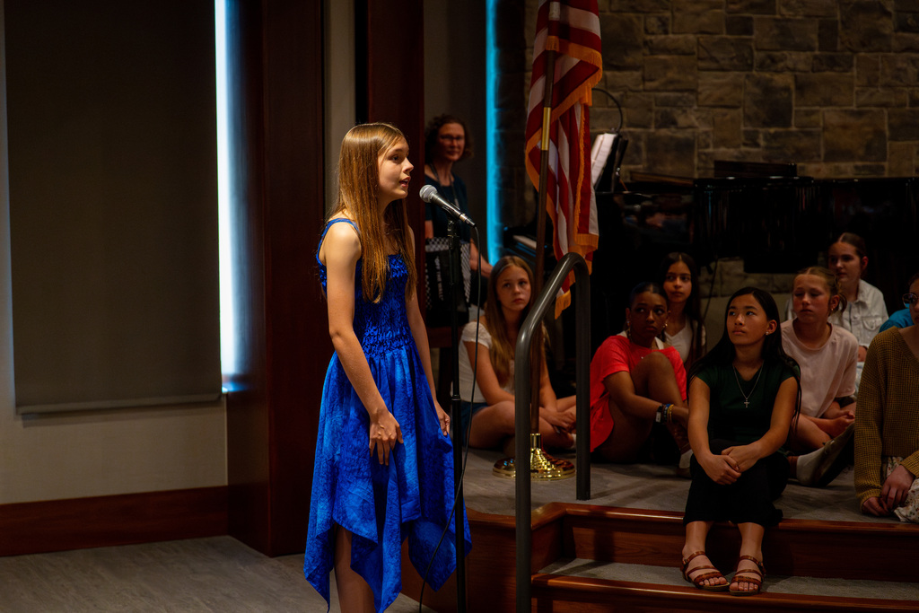 Girls choir member singing as rest of choir watches