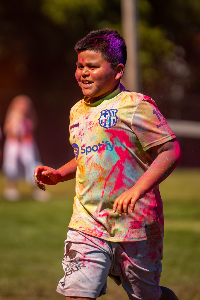 Boy in tie-dye shirt with purple hair running on grass with a colorful paint stain on his arm.
