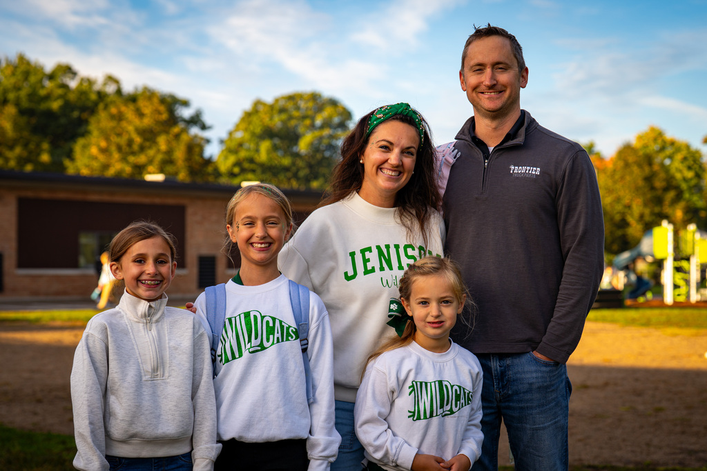 Family in white and green shirts posing in front of a building with trees.