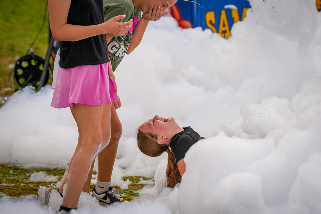 Three people near a large pile of foam. Two people stand, one laughs on the ground.