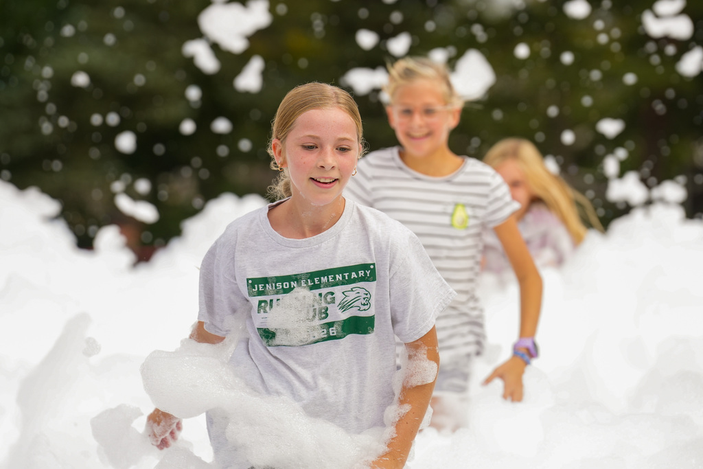 Three children in foam-filled area, one in white shirt, another in striped shirt. Trees in background.