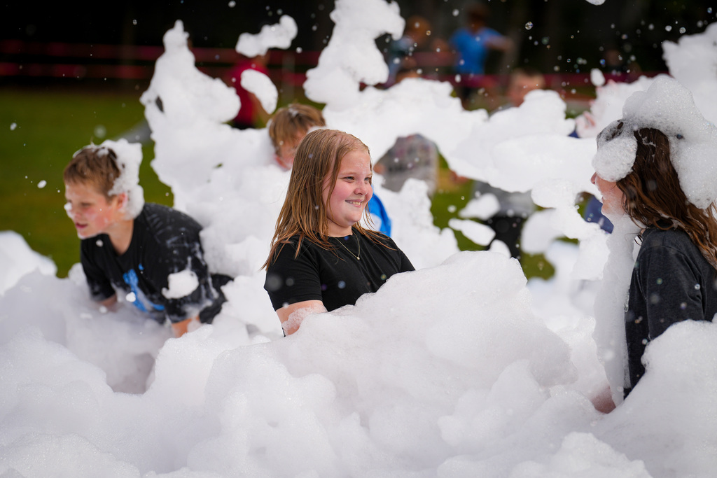 A group of children in black shirts playing in a large pile of white bubbles outside.