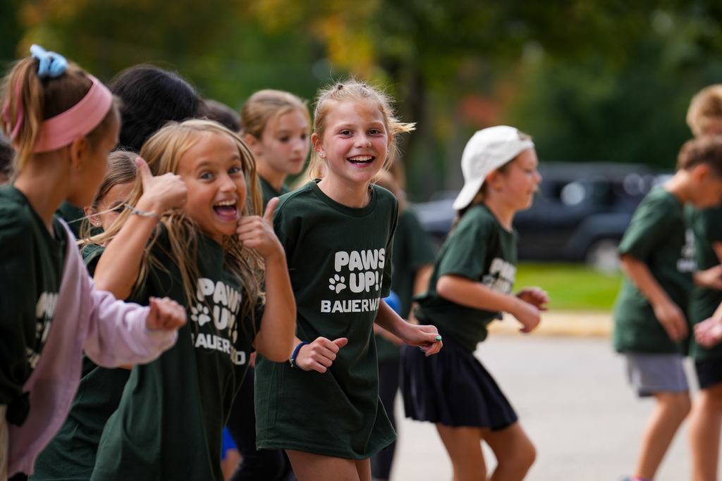 Group of young girls in matching green shirts and headbands running, one with a pink headband.
