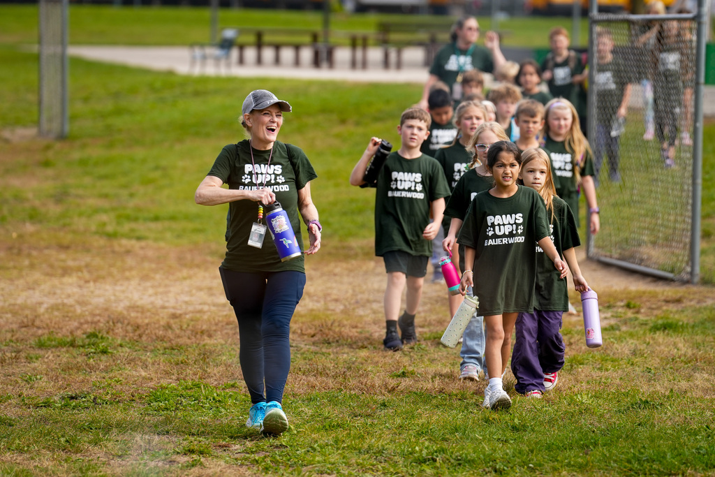 An adult and several children in matching shirts walk across a grassy field.