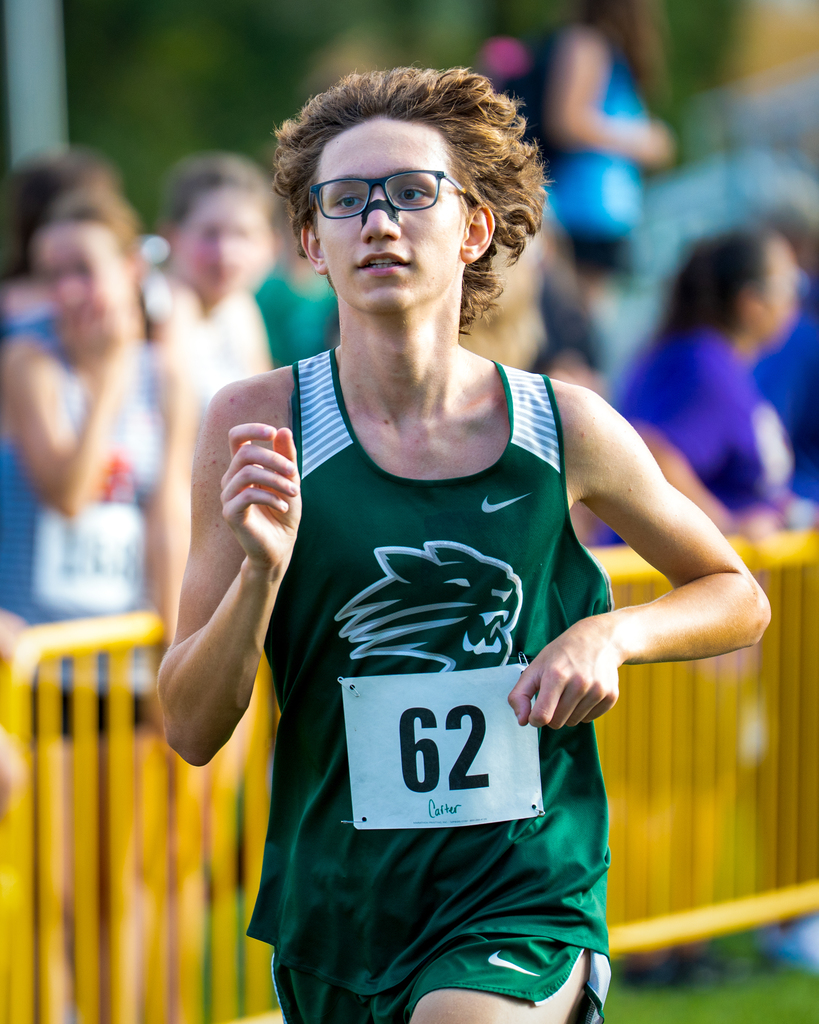 Carter Cooke in a green running uniform with the number 62 runs in a cross-country race.
