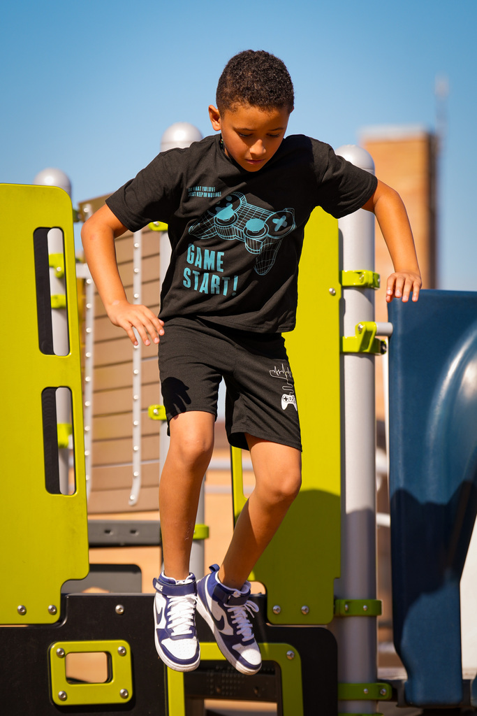 A child in a black shirt and shorts plays on a playground. He jumps over obstacles with sneakers.