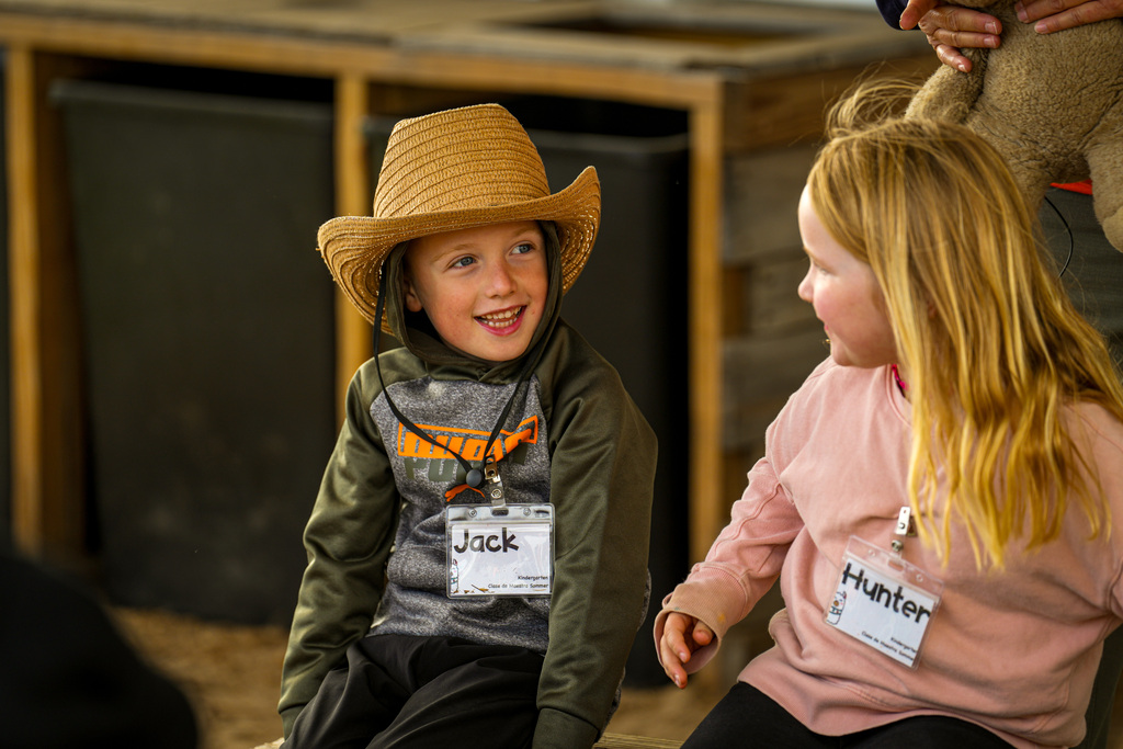 Two children smiling, one in hat, both wearing name tags.