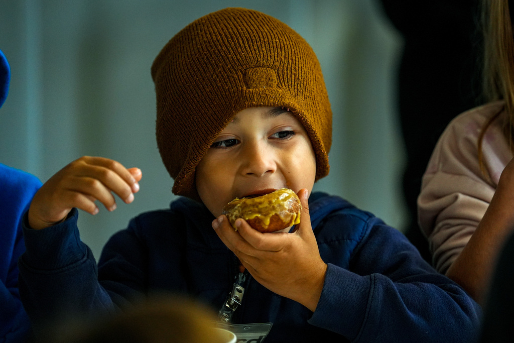 A child wearing a brown beanie eats a pastry while seated at a table.