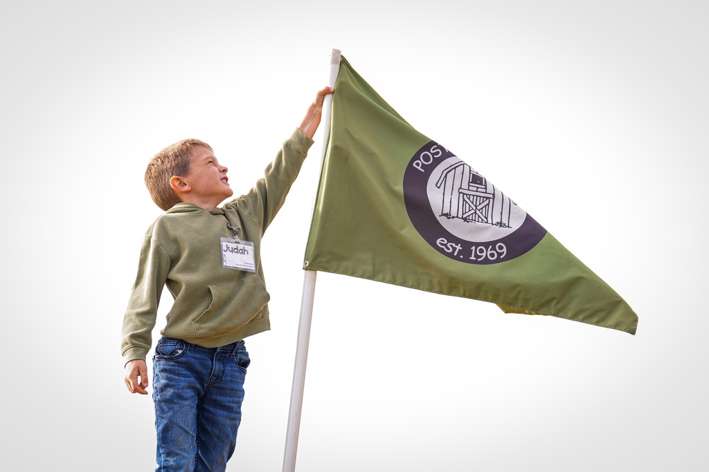 A child holds a pole with a Post Family Farm flag on it and looks up, possibly in an outdoor setting.