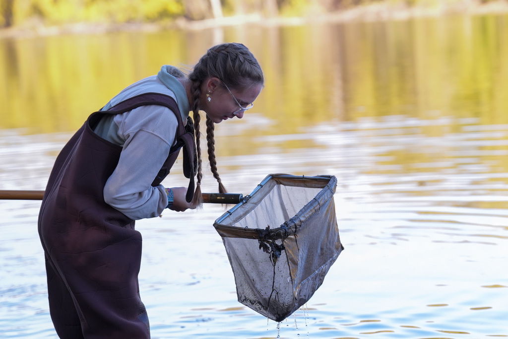 Student in a brown smock holding a mesh net in a body of water.