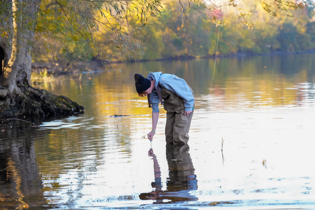 Student in water holding a tool, surrounded by trees and a body of water.