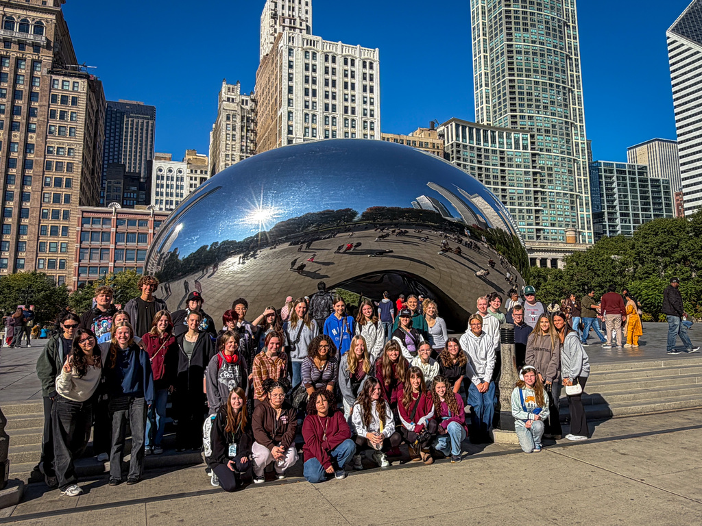 A group of students poses in front of the bean sculpture in an urban setting.