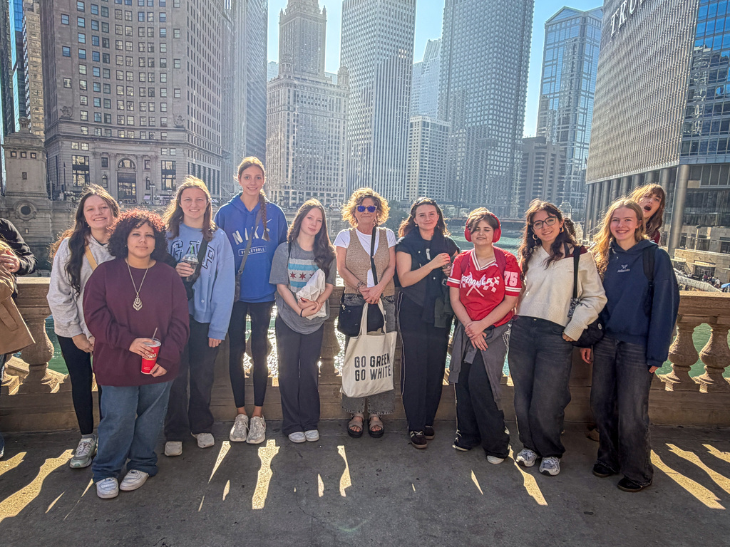 A group of students and staff stand on a bridge with a cityscape in the background.