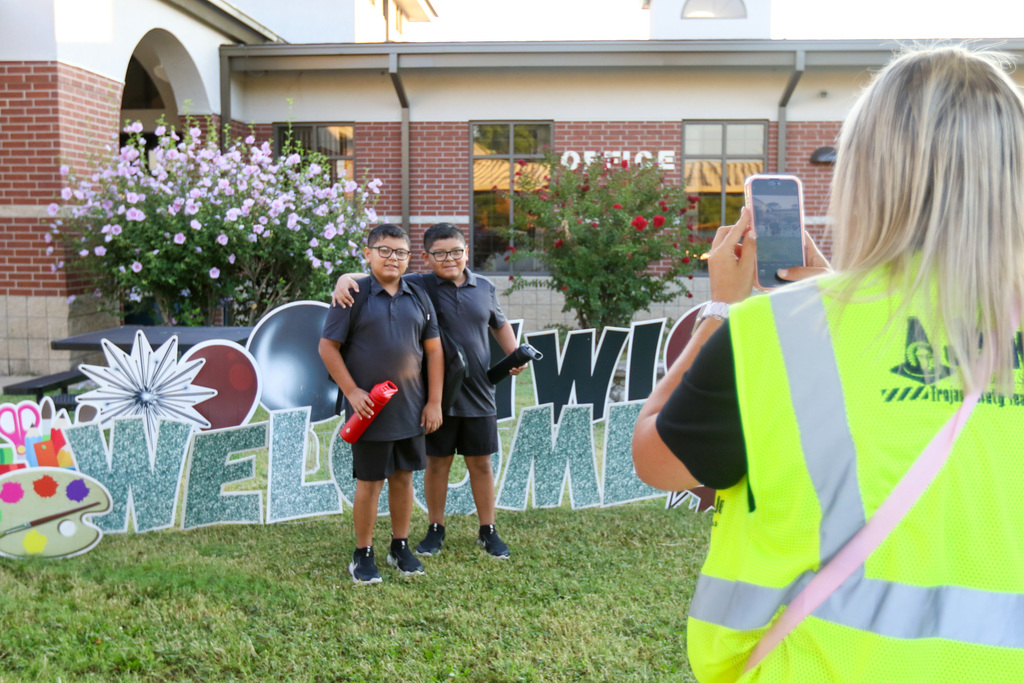 two boys getting their photo taken by a teacher by some signs