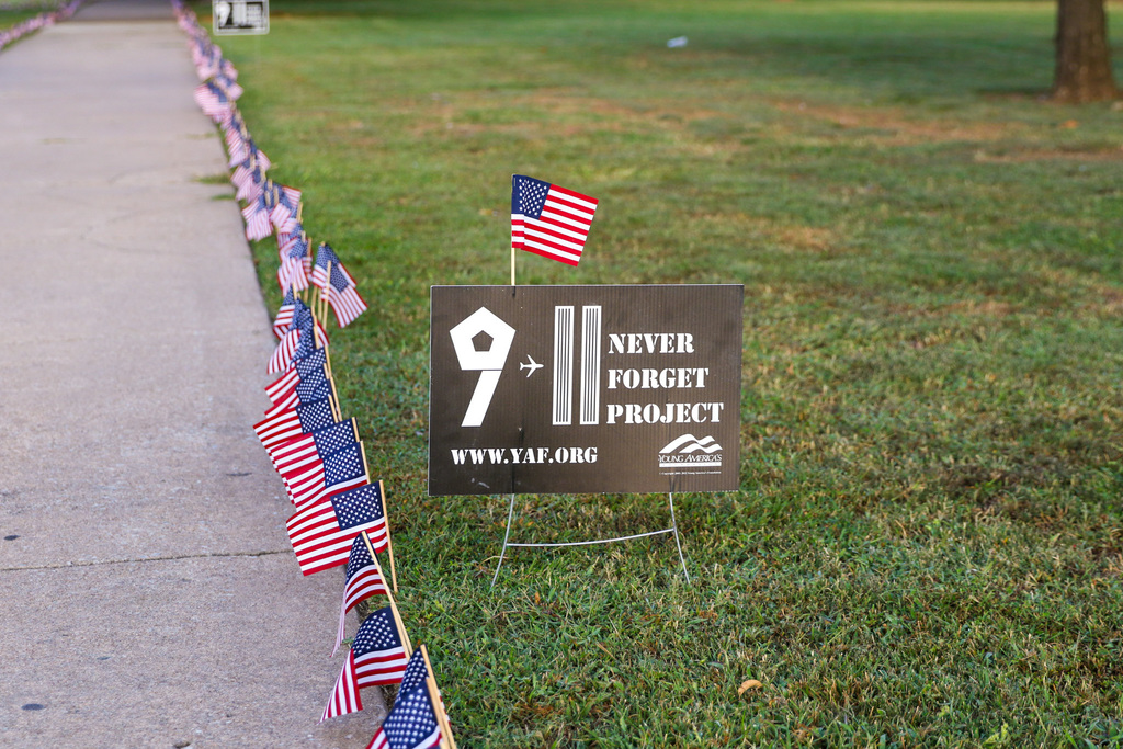 a photo of their sign that says 9/11 never forget project along with the long line of flags down the sidewalk
