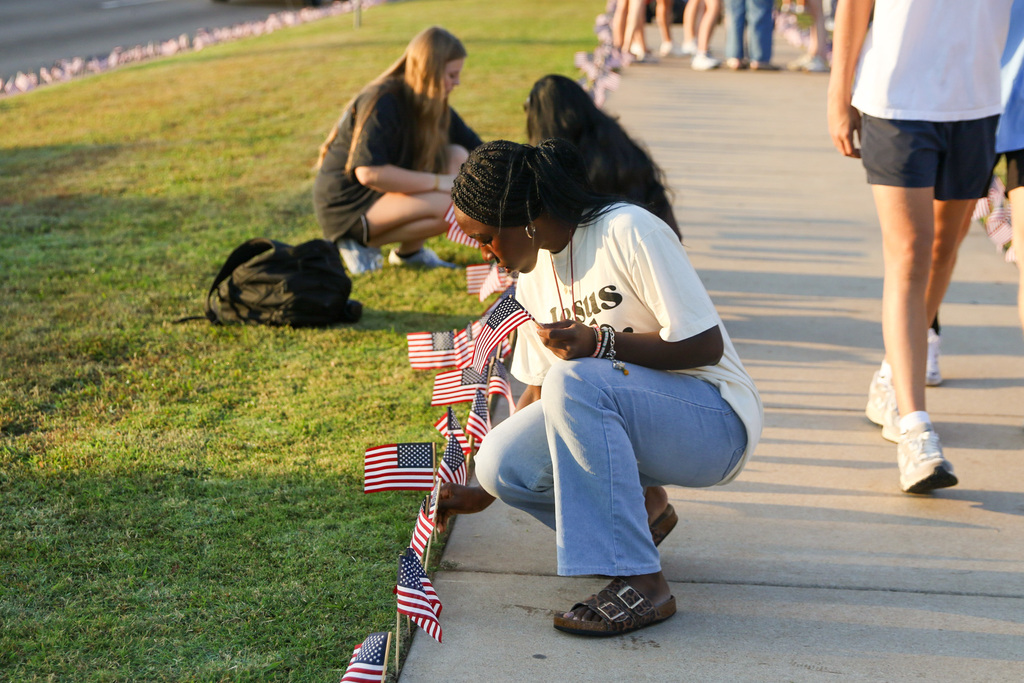 student putting flags in ground to honor lives lost. in the background there are more students doing the same thing along with the lines of flags lining the sidewalk