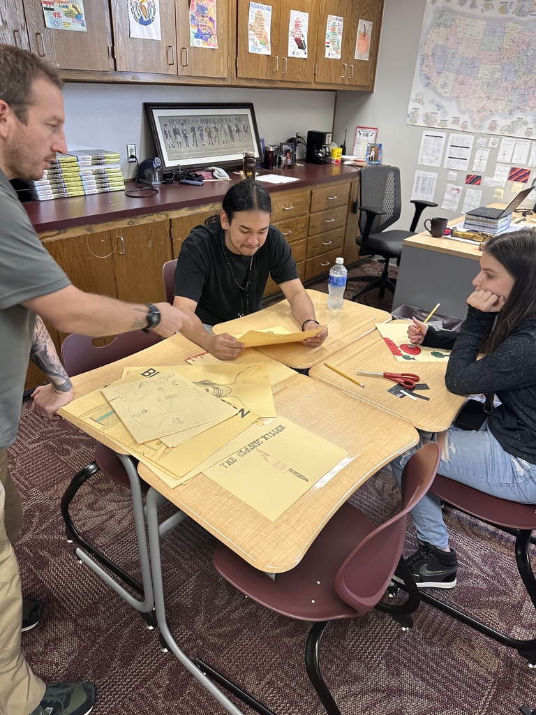 Teacher with two students at a group of desks, looking at papers