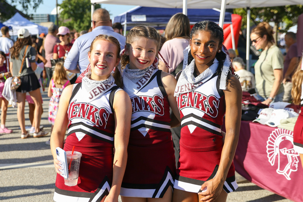3 cheerleaders standing posing for a photo infront of tables
