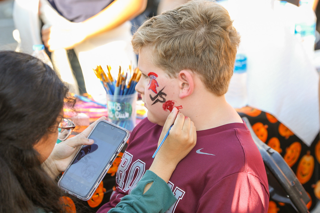 student panting a childs face. design is a spartan head vs. a trojan head