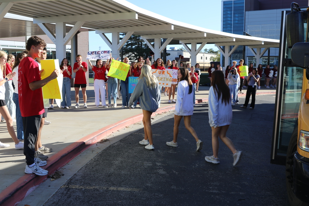 students getting off bus at Jenks High School being welcomed by signs, cheerleaders, and excited students
