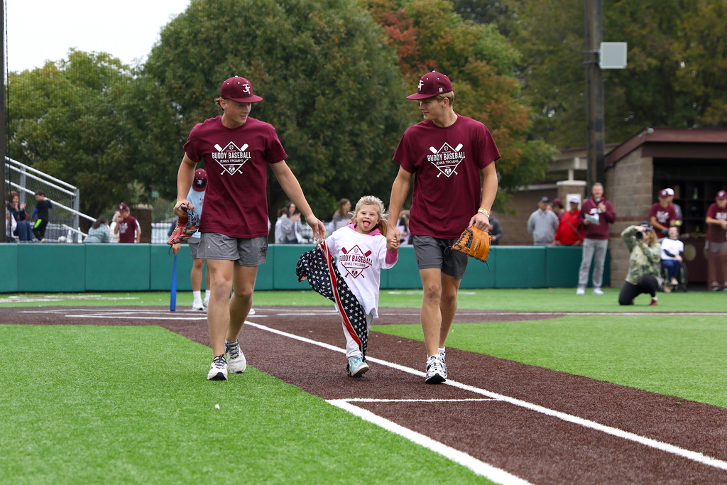 baseball players holding girl by the hand and walking down first base line