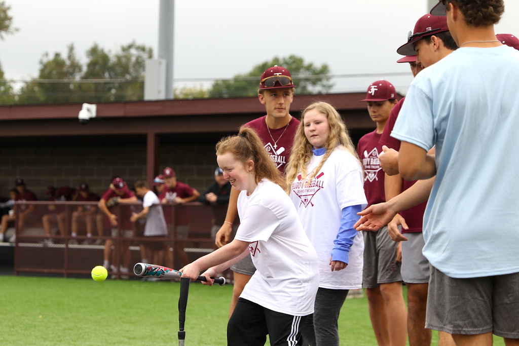 girl knocking ball off tee with bat during buddy baseball game