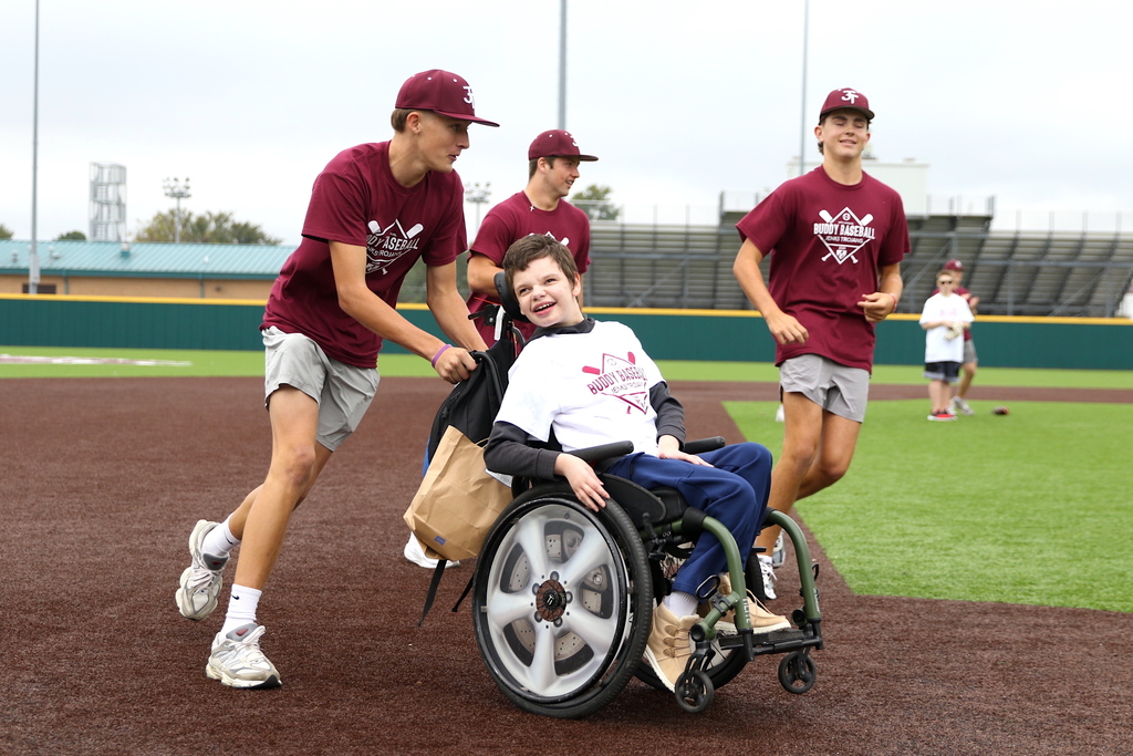 baseball players pushing buddy baseball player around the bases in a wheelchair