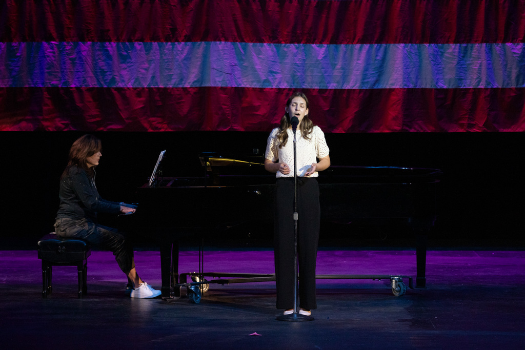 high school student singing on stage with a piano being played behind her 
