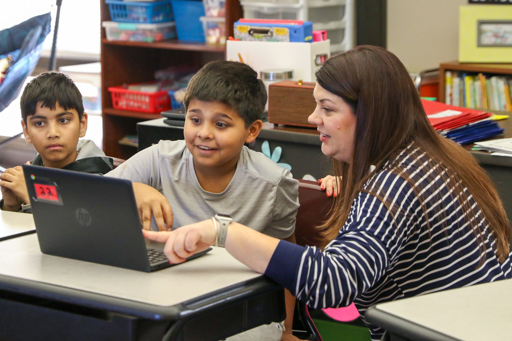 student smiling at his computer with his teacher next to him smiling and pointing at his screen