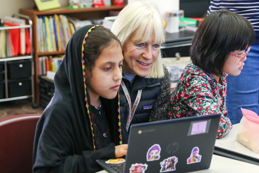 student working along side at teacher on her computer