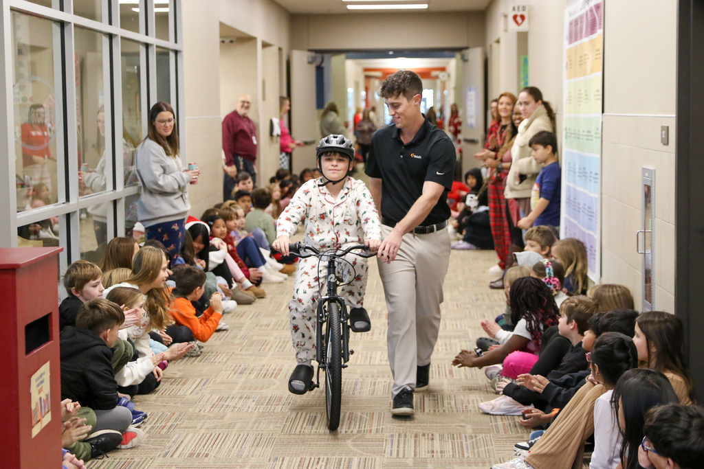 student riding down a hallway on their new bike with the help of a swerve member