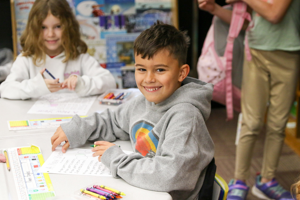 boy smiling at the camera sitting at his desk