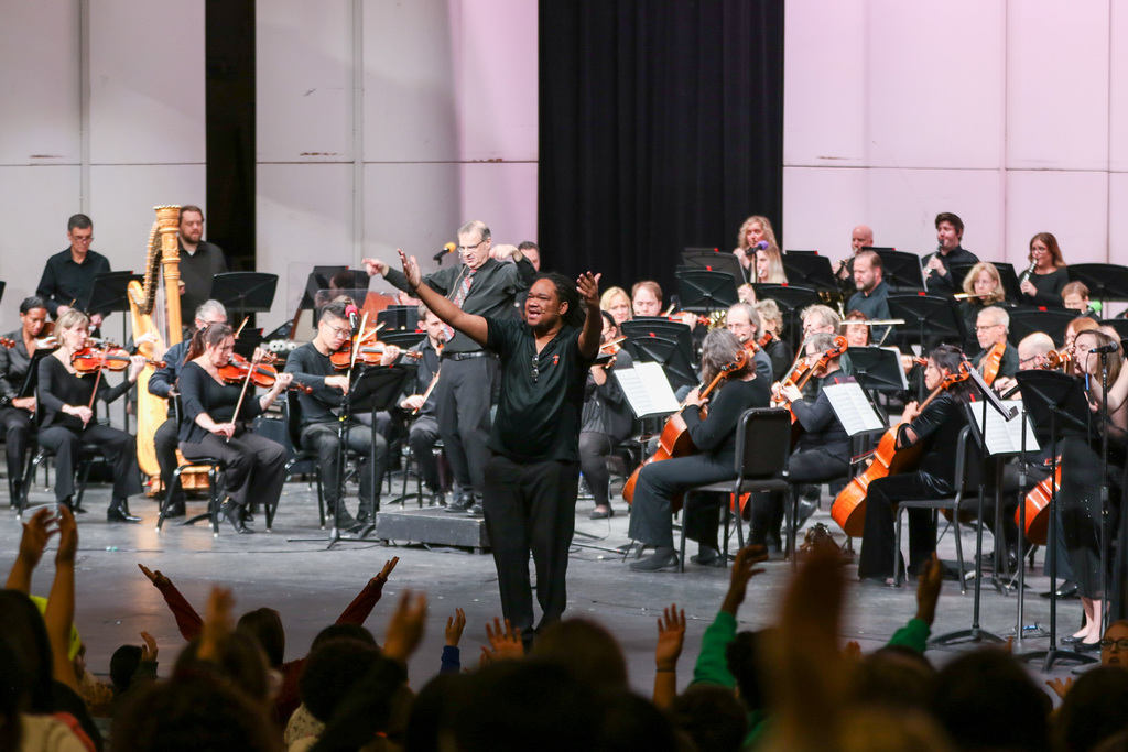 emcee on the stage singing along with the orchestra behind him. you can see hands up from kids 