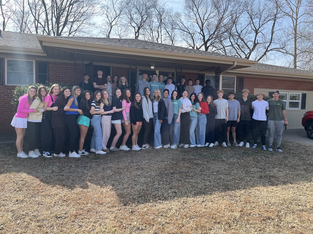 Group photo of at least 20 high school students in front of a home they helped prepare for veterans to move in