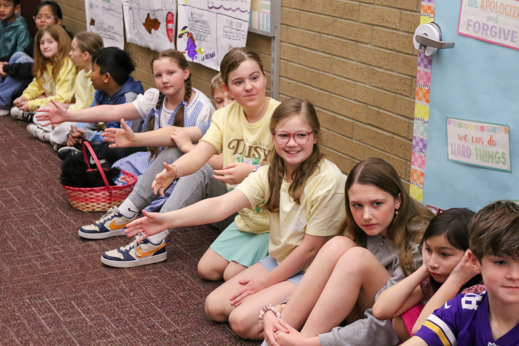 students sitting on the ground with their hands out so others can high five them