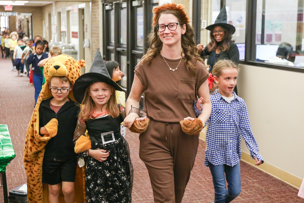a teacher and 3 students hand in hand all dressed like characters fro the wizard of oz