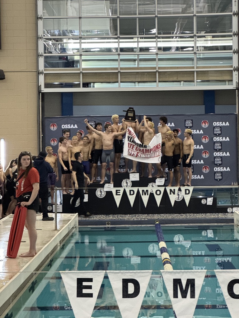 Jenks' boys swimmers standing on podium holding state championship banner