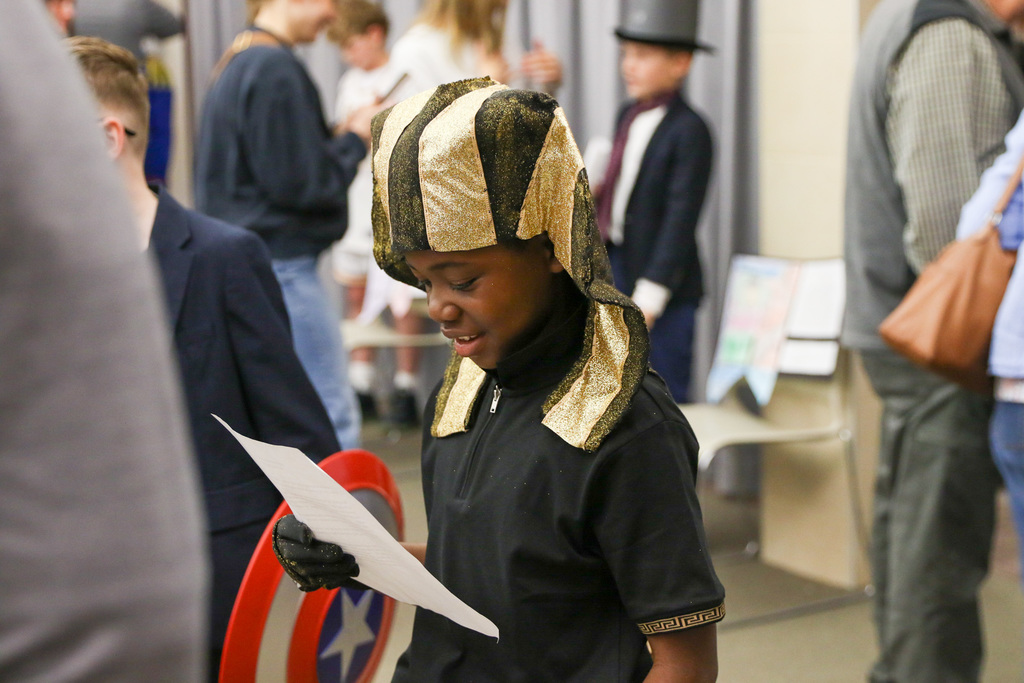 Boy dressed up as King Tut reading off a paper while presenting.