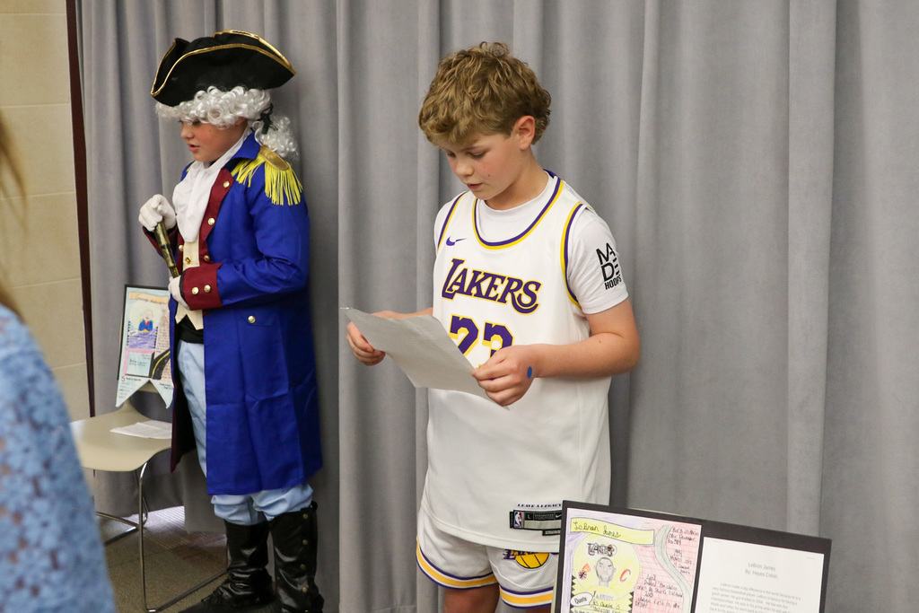 Two boys dressed up as George Washington and LeBron James, presenting their projects.