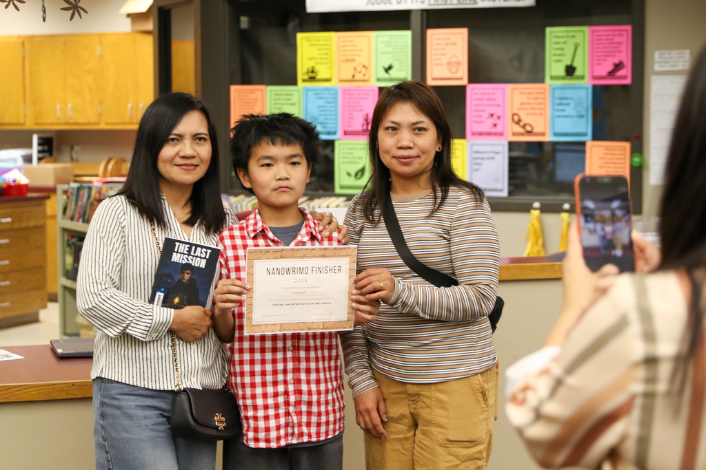Boy posing with his family for a photo. Family is holding up his book and this NaNoWriMo finisher certificate.