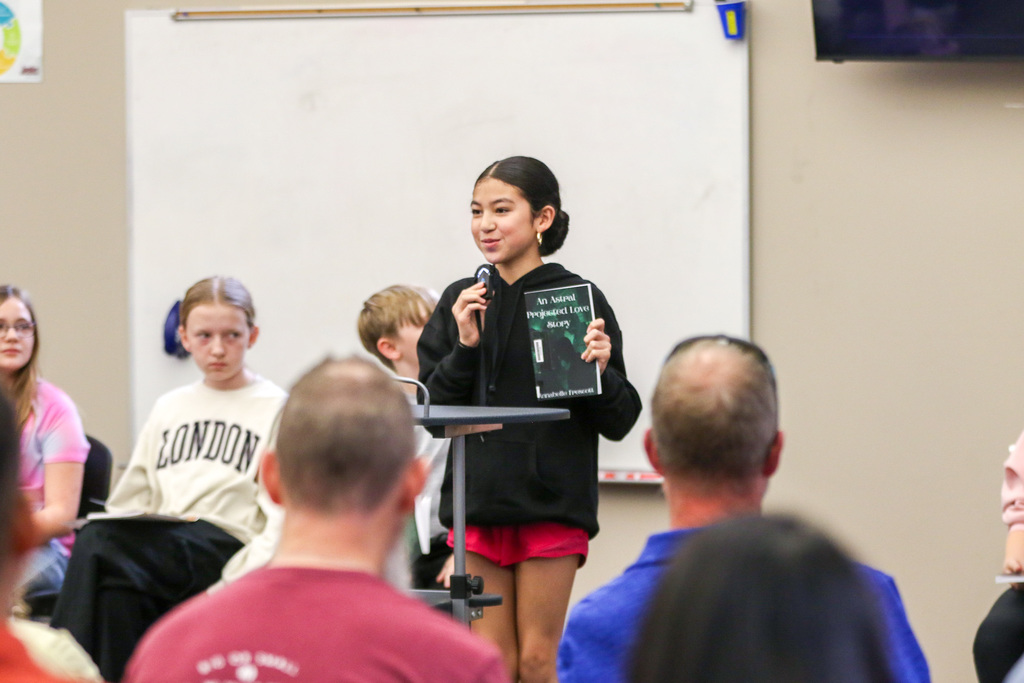 A girl standing with her book, presenting the title and reading the back summary.