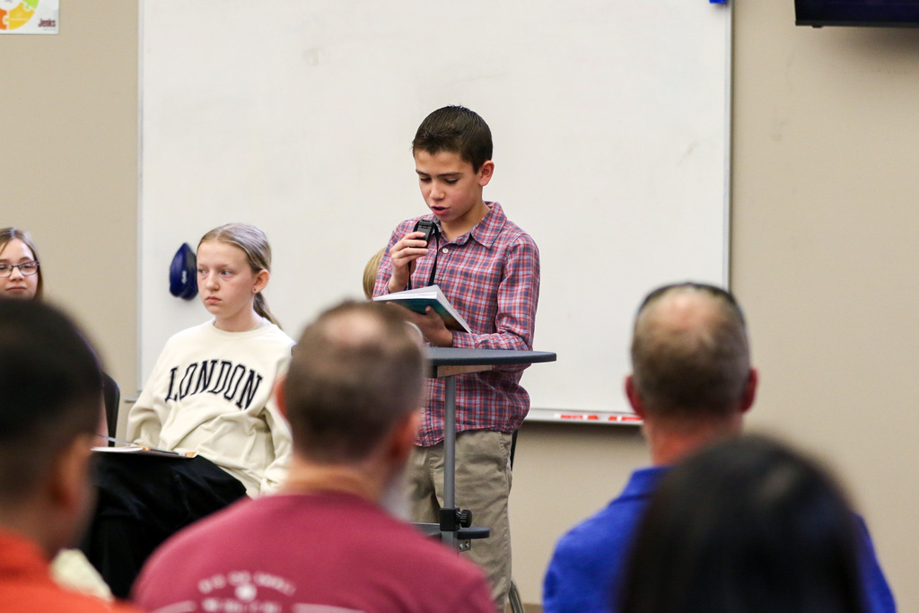 Boy reading the back of his book to the family in the crowd.
