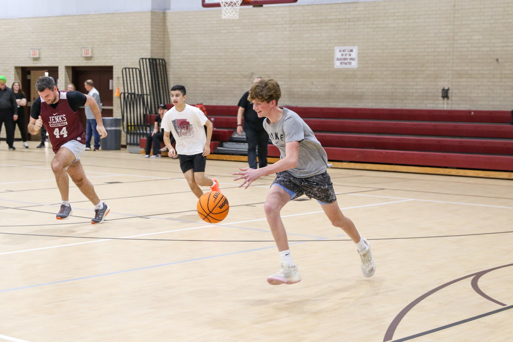 Boy dribbling the ball with a teacher and another student running beside him.