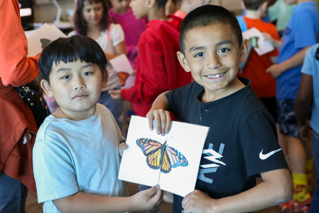 Two boys holding halves of a picture of a butterfly smiling.