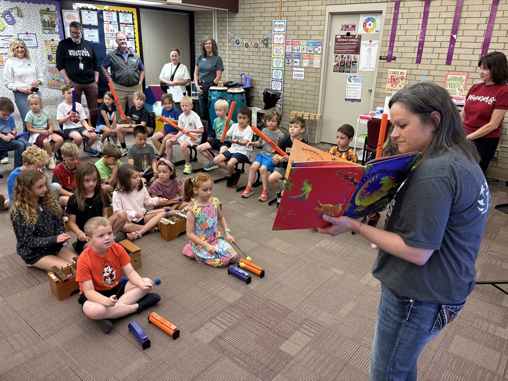 Music teacher at front of classroom as students listen and prepare to play instruments on cue