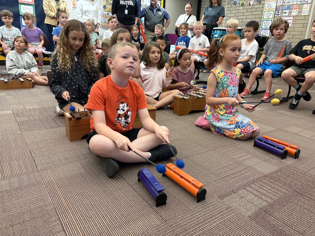 Students on floor of music room watching and listening to teacher