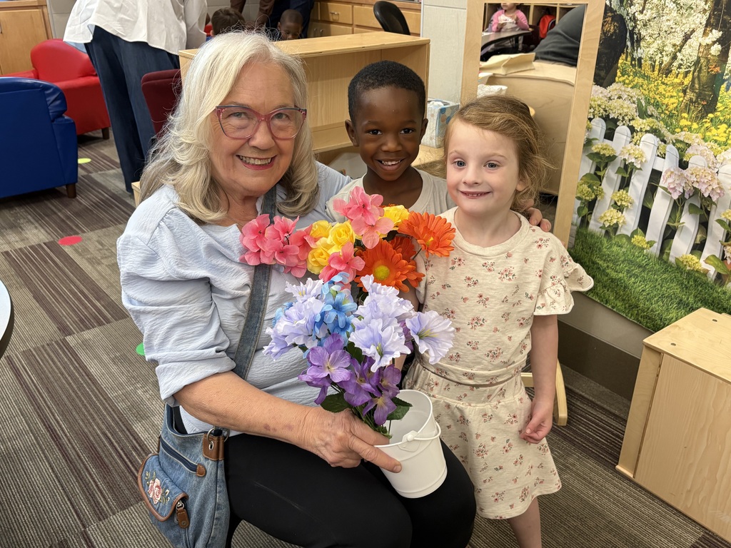 Senior living resident holding flowers next to boy and girl Pre-K students